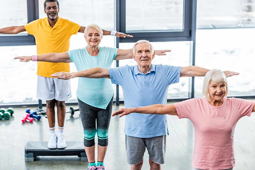 High angle view of multicultural senior athletes synchronous exercising on step platforms at sports hall