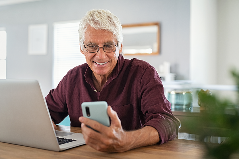 Mature man using smartphone in front of laptop