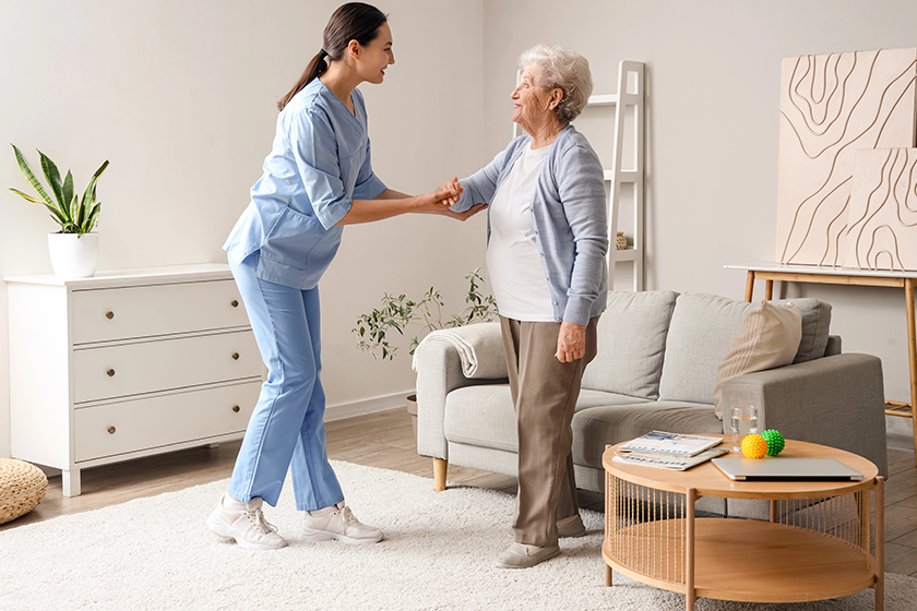 Physical therapist helping senior woman to walk at home 