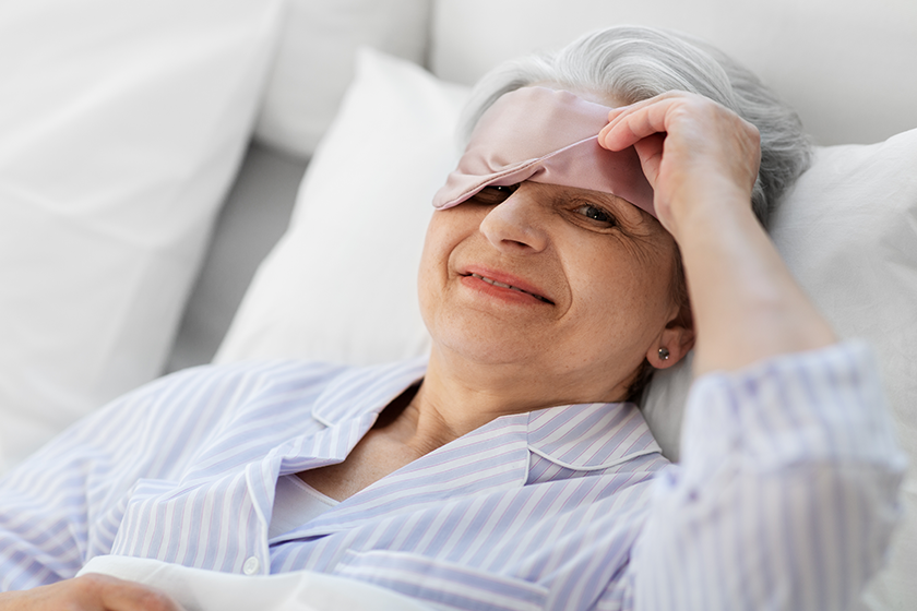 Senior woman with eye sleeping mask in bed